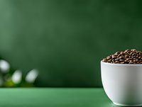 Coffee beans in white ceramic bowl on green surface with copy space for advertising and packaging design.