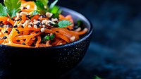 Fresh carrot salad with herbs and seeds in black bowl on dark background, healthy vegetarian meal ready for serving and cooking projects.