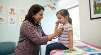 Female pediatrician examining young girl patient with stethoscope in colorful medical office during routine checkup appointment.