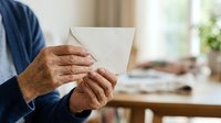 Mature man with dark skin tone holding blank white envelope in office workspace, suitable for business communication, mail delivery, correspondence, and professional messaging concepts.