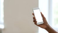 Close-up of hand holding smartphone with blank white screen for app mockup, web design, or marketing content display in modern interior setting.