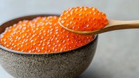 Fresh red caviar in ceramic bowl and wooden spoon against gray background, bright orange salmon roe close up view for gourmet food design.