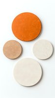 Minimalist ceramic coasters in orange and neutral tones arranged on white background, featuring textured matte finish and circular shapes for modern home decor.