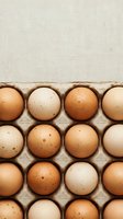 Fresh organic eggs in cardboard carton with natural speckled shells and neutral beige background for cooking and baking concepts.