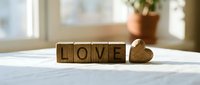 Wooden letter blocks spelling LOVE with a small carved heart on a white surface, warm sunlight in background, romantic home decor concept.