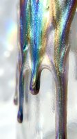 Iridescent holographic glitter dripping down white surface, creating colorful liquid streams with rainbow reflections and sparkle effects for design projects.