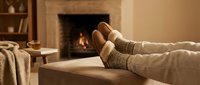 Cozy winter evening at home with feet in warm wool socks resting on coffee table near fireplace. Relaxation and comfort concept for cold season lifestyle.