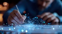 Businessman writing with pen on digital surface with glowing blue particles, creating futuristic data visualization effect in dark office environment.