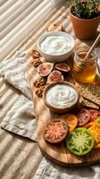 Wooden board with fresh figs, walnuts, honey jar, yogurt bowls and colorful tomato slices on rustic table with natural sunlight shadows for healthy eating.