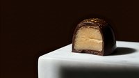 Gourmet chocolate truffle with golden filling cut in half, displayed on white surface against dark background for luxury confectionery and food photography.