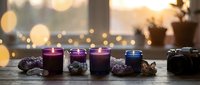 Colorful scented candles in glass jars arranged on wooden surface with warm bokeh lights creating cozy atmospheric home decor for relaxation and aromatherapy.