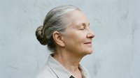 Mature woman with gray hair in bun, fair complexion, wearing beige sweater, smiling in profile against neutral background. Suitable for healthcare, wellness, aging, lifestyle and senior-related projects.