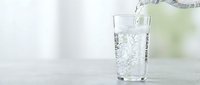 Fresh clean water being poured into transparent glass on light surface with soft natural lighting for healthy lifestyle and hydration concepts.