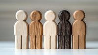 Wooden figures standing together showing diversity and inclusion concept, carved human shapes in different wood tones against neutral background.