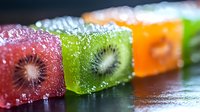 Colorful fruit jelly cubes with kiwi slices inside on dark background with water drops, macro shot showing texture and freshness of sweet dessert.