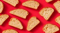 Fresh sliced whole grain bread pieces arranged on vibrant red background. Artisan bakery products with visible texture for food photography and culinary designs.