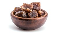 Brown sugar cubes in rustic wooden bowl on white background, crystallized raw cane sugar pieces with natural caramel color and sparkly texture.