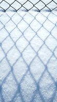 Chain link fence shadow pattern cast on fresh white snow creating geometric diamond shapes in winter sunlight for seasonal backgrounds.