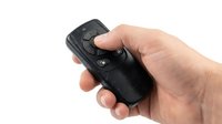Male hand holding black wireless remote control device with buttons on white background.