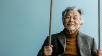 Happy senior Asian man with gray hair smiling while holding rope on blue background, expressing joy and positivity in retirement lifestyle.