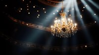 Elegant crystal chandelier illuminated by dramatic light beams in dark theater interior with bokeh lights creating atmospheric ambiance.