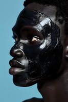 African woman in profile wearing glossy black face mask against blue background, dramatic beauty portrait highlighting skincare and cosmetic concepts.