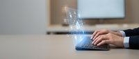 Professional businessman hands typing on laptop with digital security shield hologram projection representing cybersecurity and data protection in modern office.