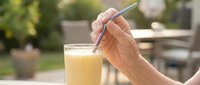 Senior adult hand holding straw in glass of fresh juice outdoors on sunny patio, refreshing beverage for healthy lifestyle and wellness.