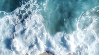 Dramatic aerial view of powerful ocean waves creating white foam patterns against turquoise water, captured from above showing natural water movement and texture.