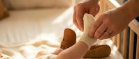 Adult hands gently putting warm knitted socks on baby feet in cozy bedroom setting with soft natural lighting for comfort and care concepts.