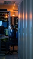 Female IT specialist working late in modern server room with glowing network equipment and data center infrastructure for technology operations.