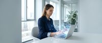 Professional businesswoman working on laptop in modern office environment with natural lighting and contemporary workspace design for corporate presentations.