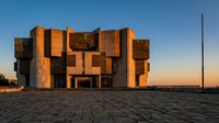 Contemporary brutalist architecture building with geometric copper and concrete facade illuminated by golden sunset light, suitable for architectural design, real estate, and modern construction projects.