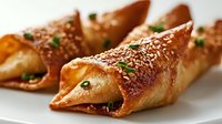 Golden crispy pastry rolls filled with savory ingredients, garnished with sesame seeds and fresh herbs on white plate for culinary presentations.
