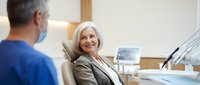 Senior woman patient smiling during dental consultation with male dentist in modern clinic office for oral health checkup and treatment planning.