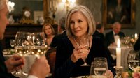 Elegant mature blonde woman enjoying wine at upscale restaurant dinner party with friends, celebrating special occasion in warm candlelit atmosphere.