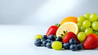 Fresh mixed fruits including strawberries, blueberries, green grapes and orange slice arranged on white surface for healthy eating and nutrition concepts.
