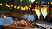 Prosciutto and olives served with sparkling wine glasses on wooden board against blurred bokeh lights background, romantic evening appetizer setting.