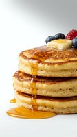 Stack of fluffy golden pancakes with maple syrup dripping down sides, topped with fresh blueberries and raspberry on white background for breakfast menu design.