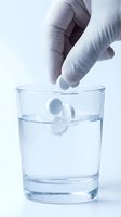 Gloved hand dropping effervescent tablet into glass of water, dissolving medication concept for healthcare and pharmaceutical use.