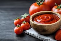 Fresh homemade tomato sauce in wooden bowl with ripe red tomatoes on dark background, traditional Italian cuisine preparation for pasta and pizza.