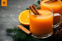 Hot spiced orange drink with cinnamon sticks and fresh citrus fruit served in glass mug on dark background with winter decorations and star anise.