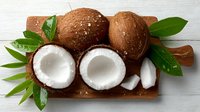 Fresh coconuts with green leaves on wooden cutting board, tropical fruit arrangement for healthy cooking and natural food concepts.