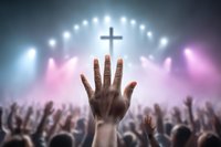 Raised hand reaching toward glowing cross with crowd of worshippers in atmospheric lighting at church service, spiritual moment of praise and worship.