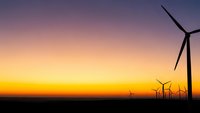 Wind turbines silhouetted against dramatic sunset sky with purple and orange gradient colors creating renewable energy landscape for sustainable power generation.