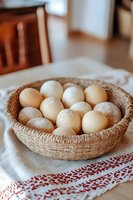 Fresh farm eggs in rustic woven basket on embroidered linen cloth, warm natural lighting creates cozy kitchen atmosphere, soft focus composition.
