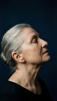 Serene senior woman with gray hair looking up peacefully against dark blue background, expressing hope, meditation and inner strength in profile view.