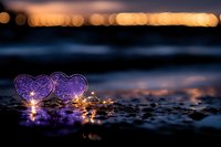 Purple heart-shaped lights glowing on wet beach sand at sunset with bokeh background for romantic Valentine's Day concepts and love themes.