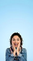 Young woman with dark curly hair and olive complexion expressing surprise and excitement with hands on face against light blue background for advertising and promotional campaigns.