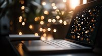 Laptop keyboard with glowing bokeh lights in dark room creating magical atmosphere. Screen reflects scattered light pattern, perfect for technology themes.